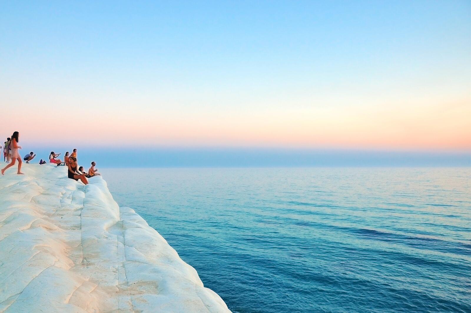 Бесплатное фото Туристы смотрят на морской пейзаж со скалы