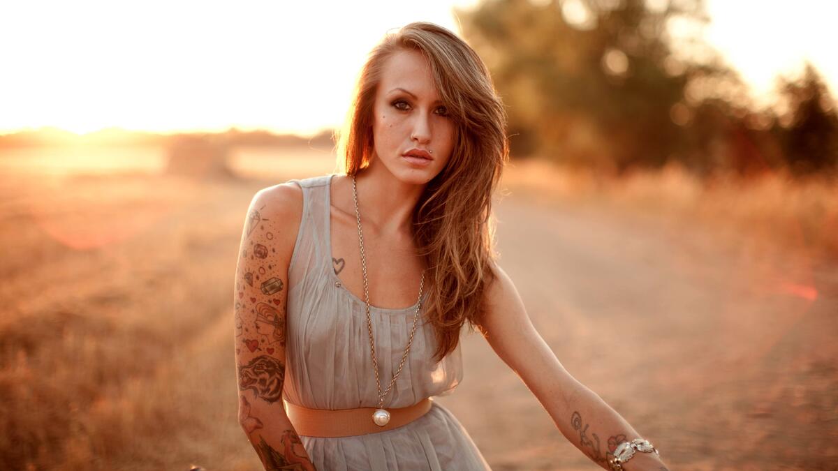 A girl with tattoos on her arms against the background of the sunset