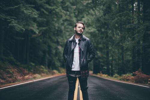 A guy in a leather jacket standing on a forest road.