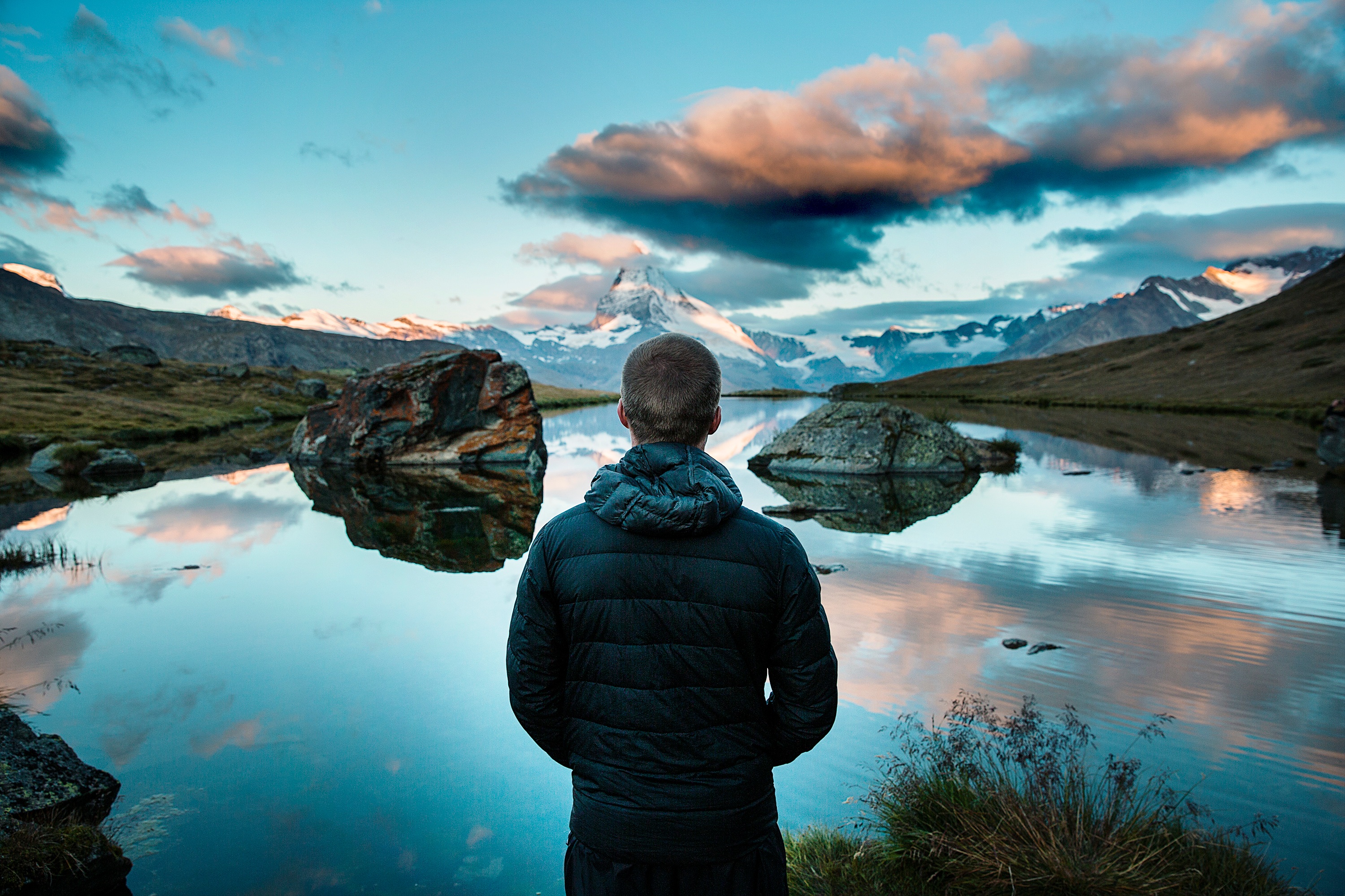 A man stands by a lake in the mountains and looks out into the distance