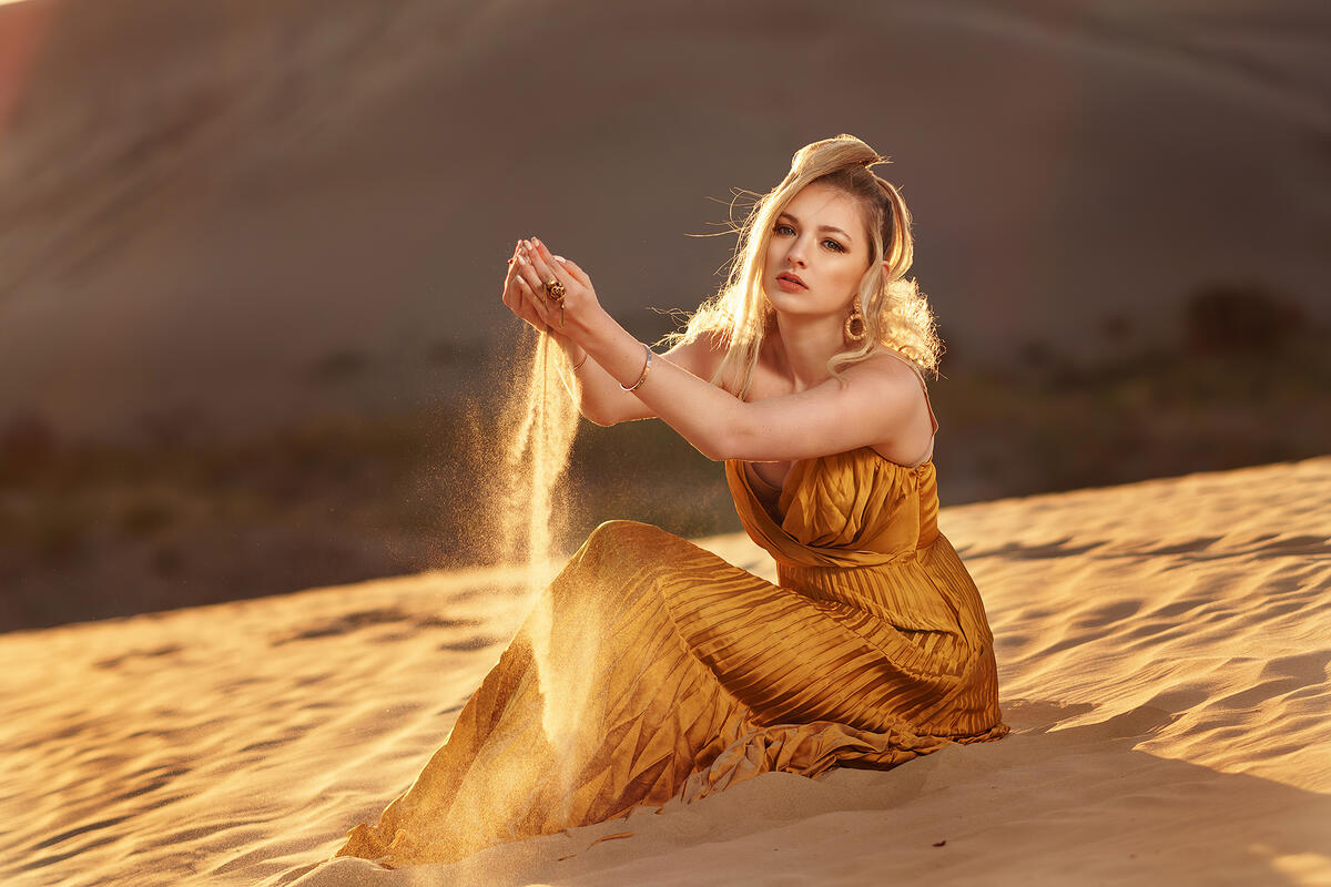 Блондинка в пустыне высыпает из ладошек песок
