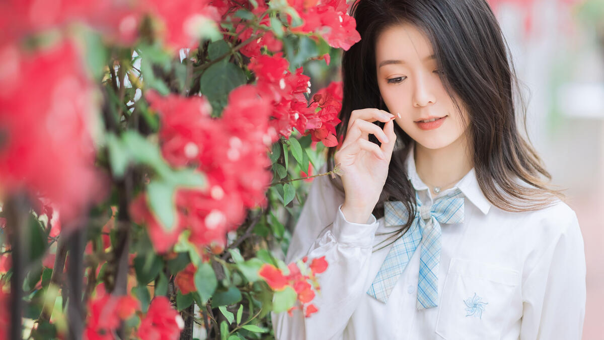 Симпатичная азиатская девушка стоит у забора с цветами