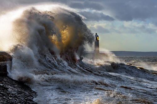 The wave breaking on the rock of the shore with the lighthouse