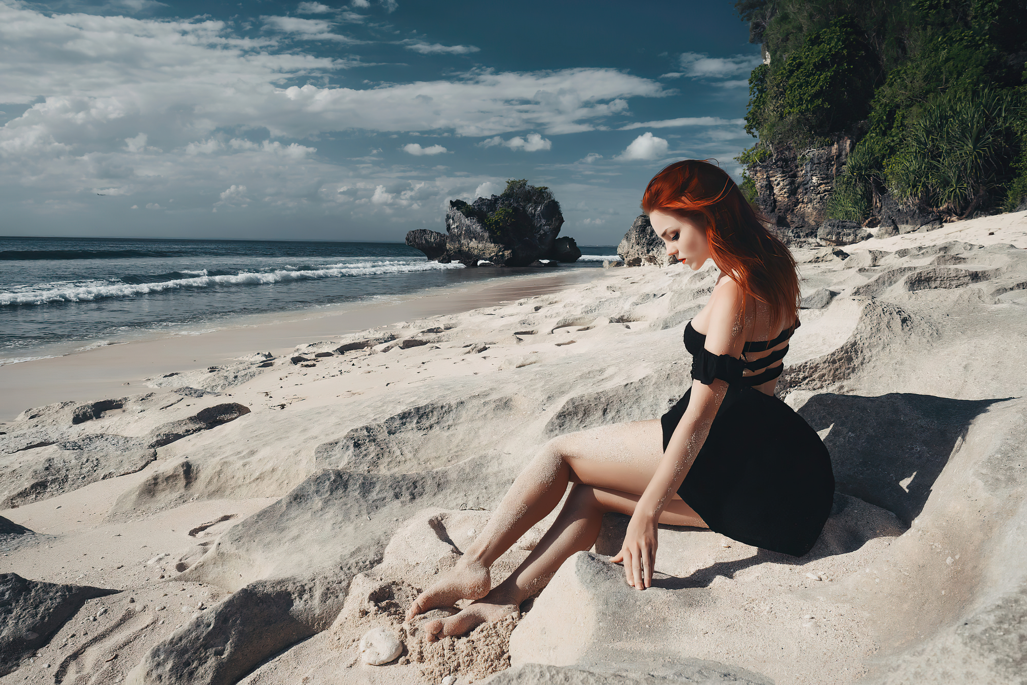 Рыжеволосая девушка сидит на песчаном пляже