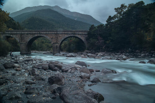 Каменный мост через реку с сильным течением в пасмурную погоду