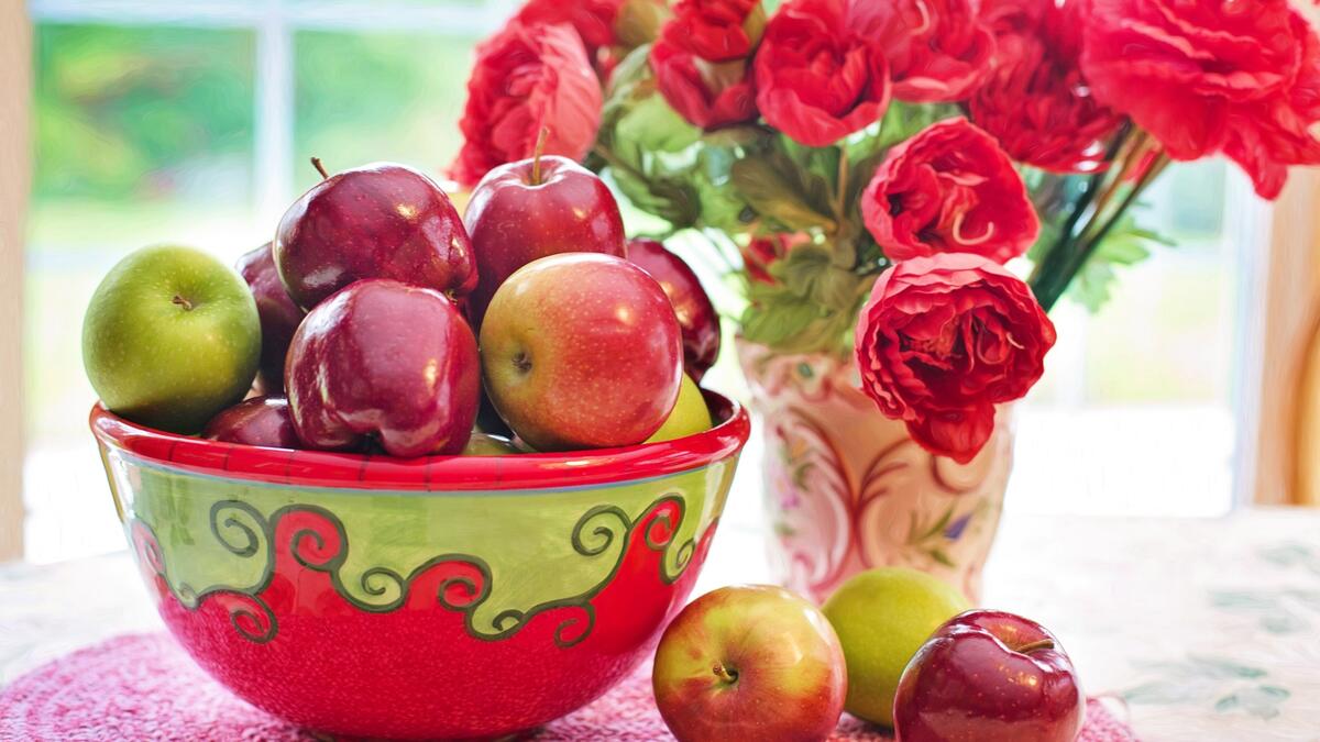 Чаша со сладкими яблоками рядом с букетом цветов красного цвета