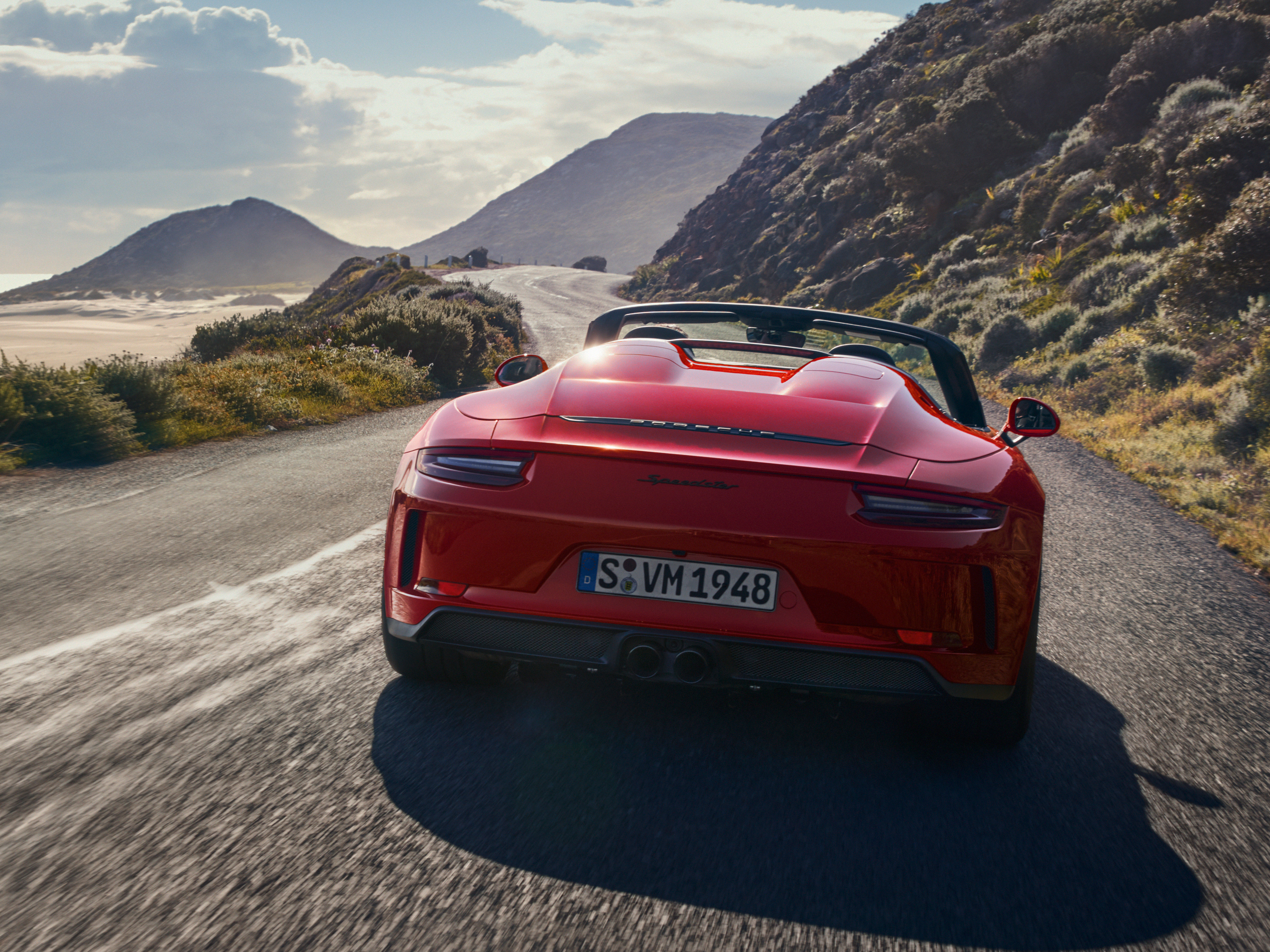 Red Porsche 911 convertible drives down the road at the foot of the mountain