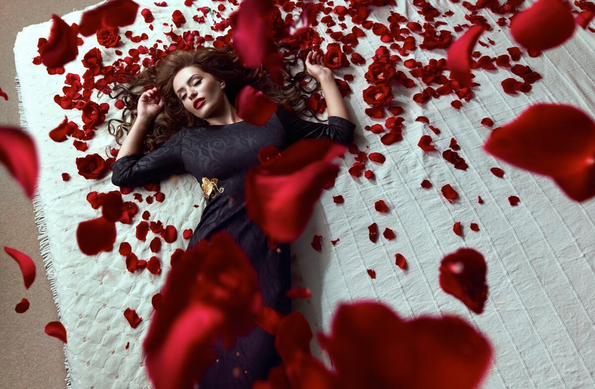 A girl in a black dress under red rose petals