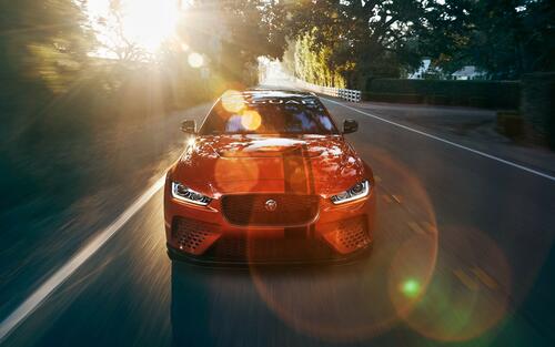 The bright orange Jaguar XE SV Project 8 drives down the road in the sunlight