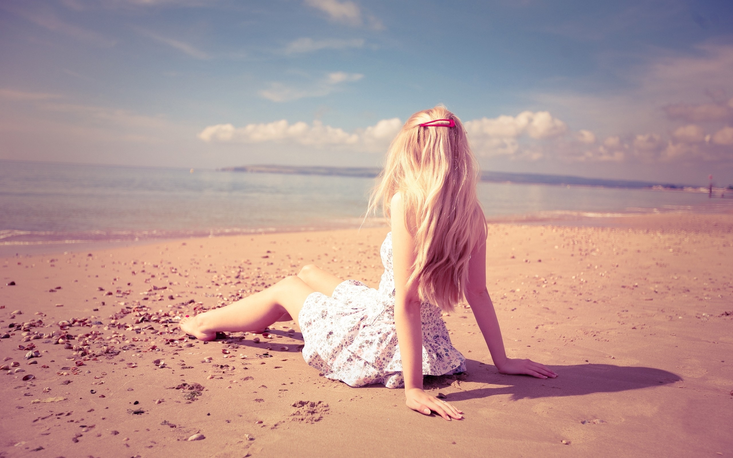 Светловолосая девушка в платье сидит на берегу моря