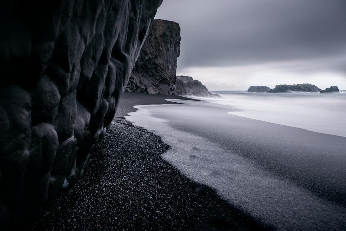 Галька на берегу у скалы на монохромном фото