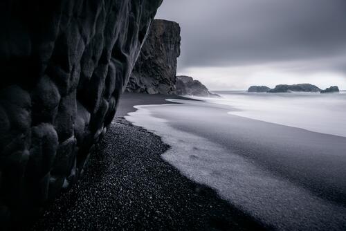Галька на берегу у скалы на монохромном фото