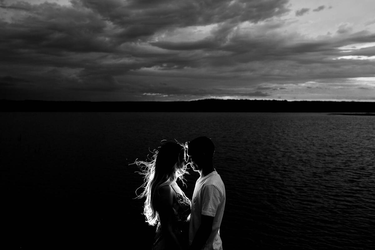 Влюбленная пара обнимается на берегу озера в темное время суток