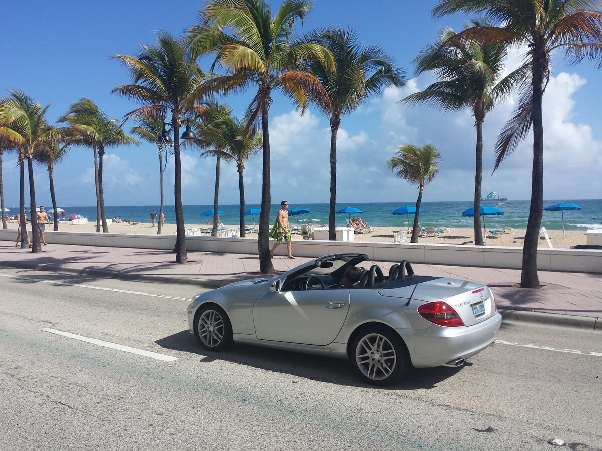Mercedes кабриолет проезжает рядом с пляжем и пальмами