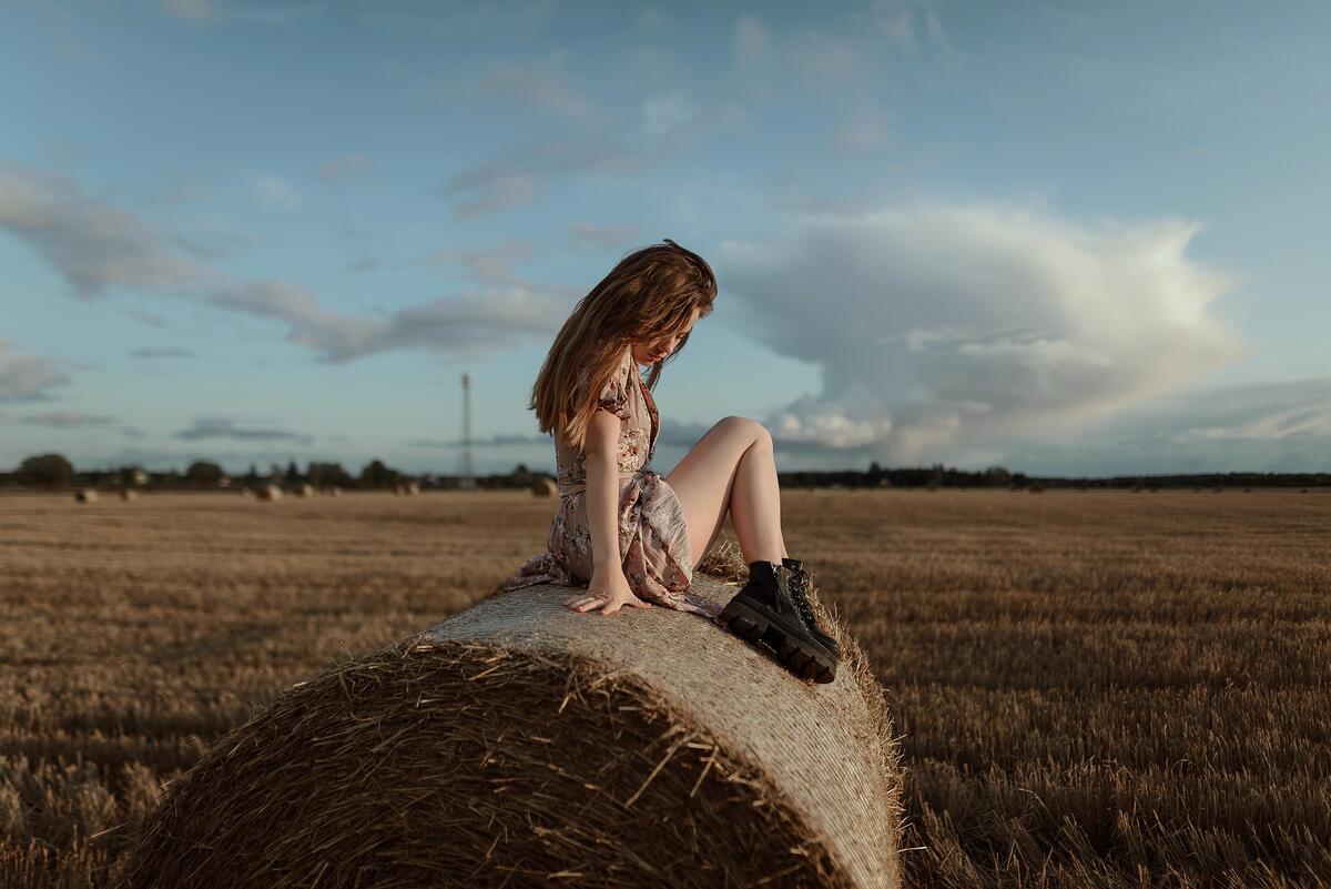 Деревенская девочки сидит на стоге сена