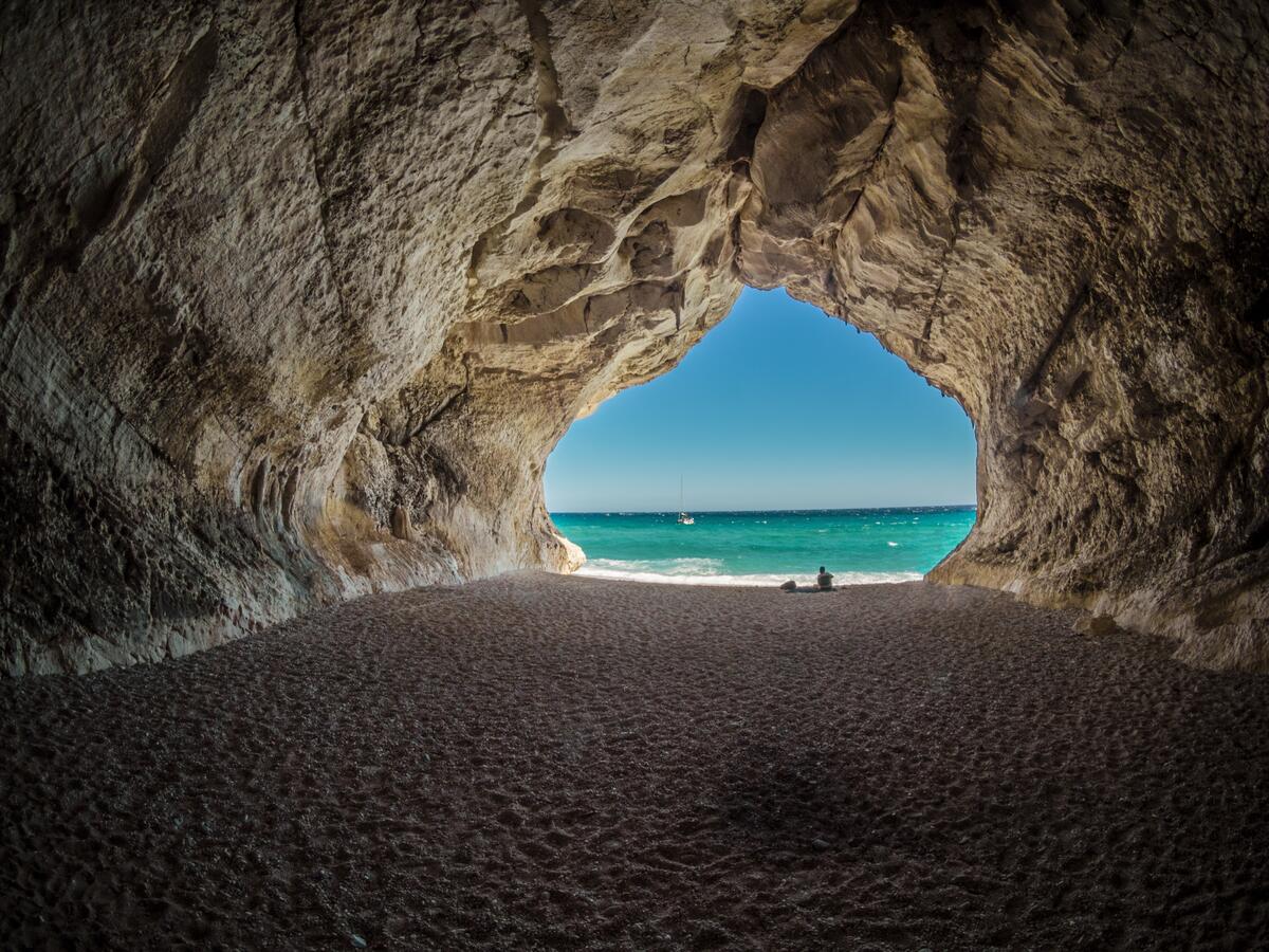 Пещера в скале с выходом на песочный пляж моря