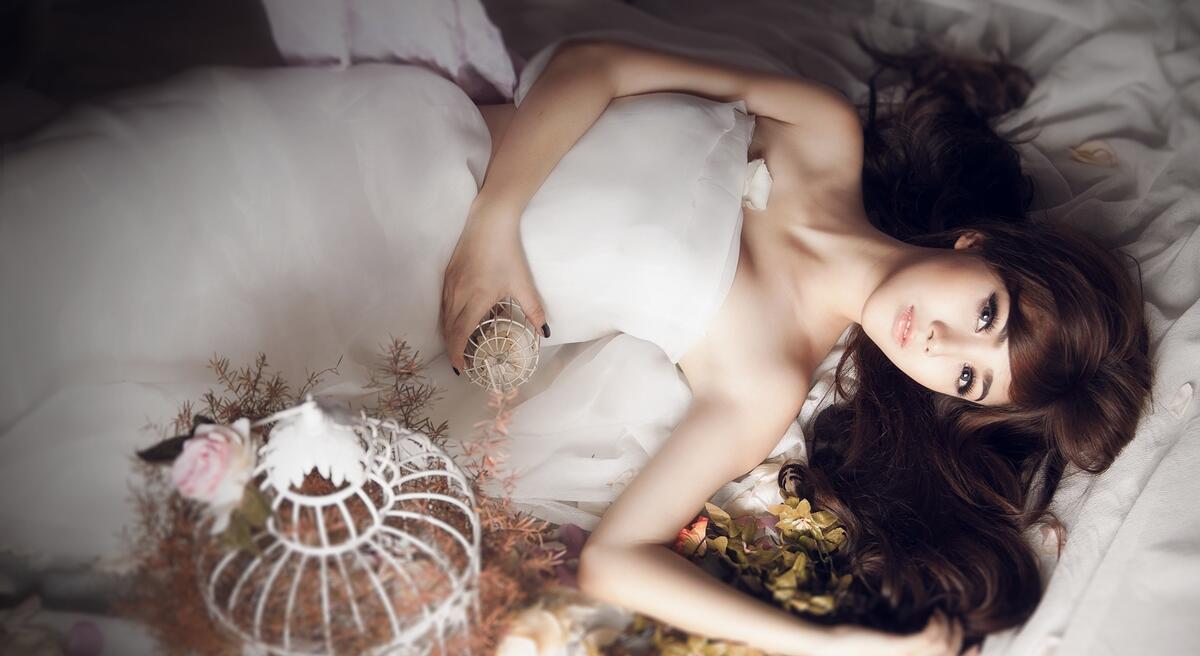 Девочка азиатской внешности в белом свадебном платье лежит на кровати