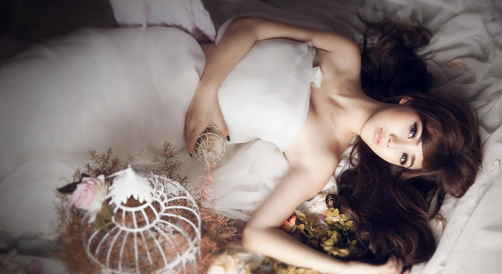 Бесплатное фото Девочка азиатской внешности в белом свадебном платье лежит на кровати