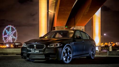 Black matte BMW M5 stands under the bridge