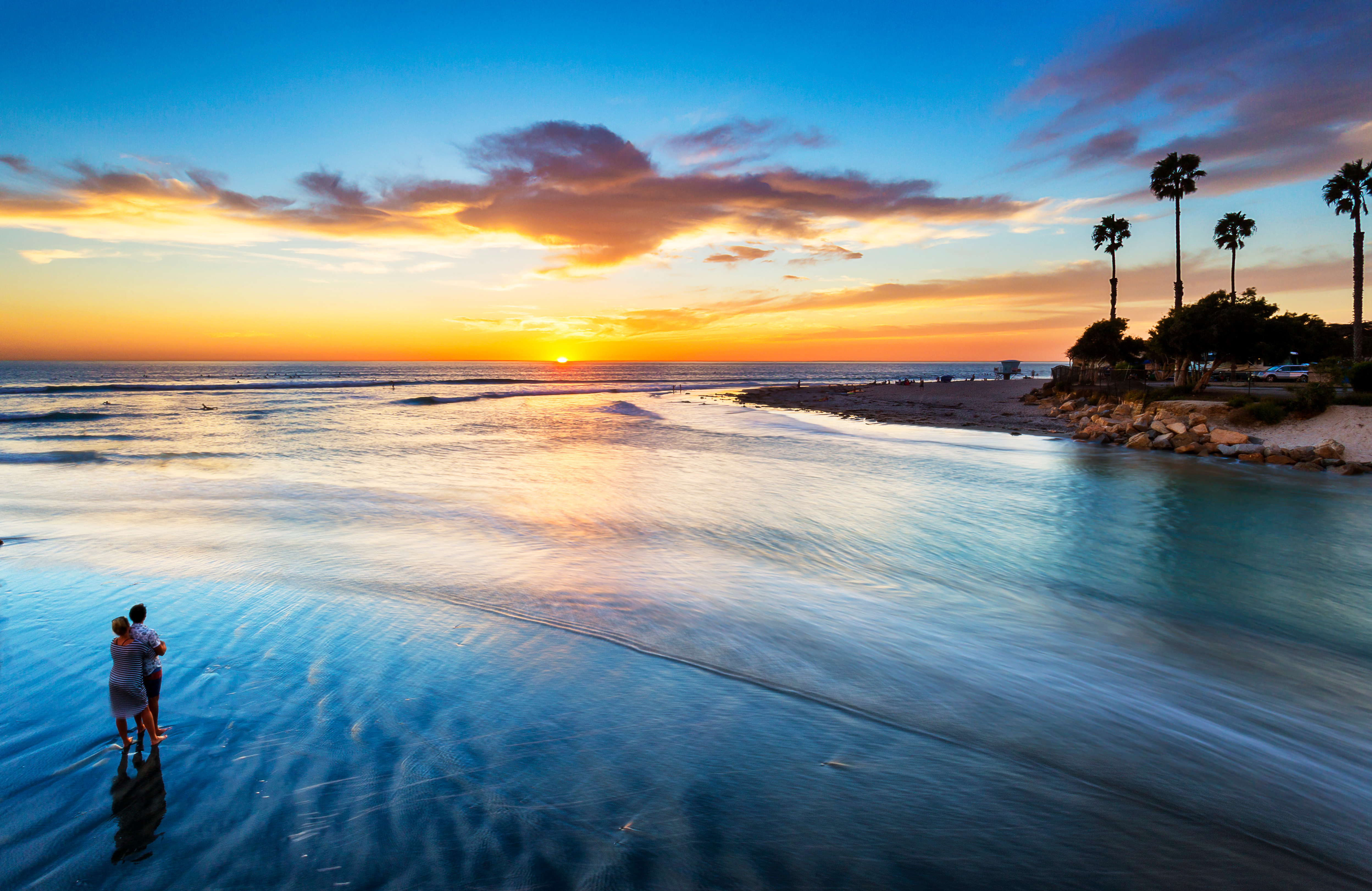 免费照片夫妇在棕榈树环绕的海滩上享受美丽的夕阳