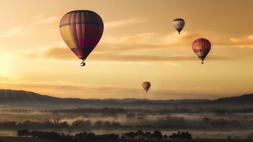 Balloons fly over a misty field at sunset