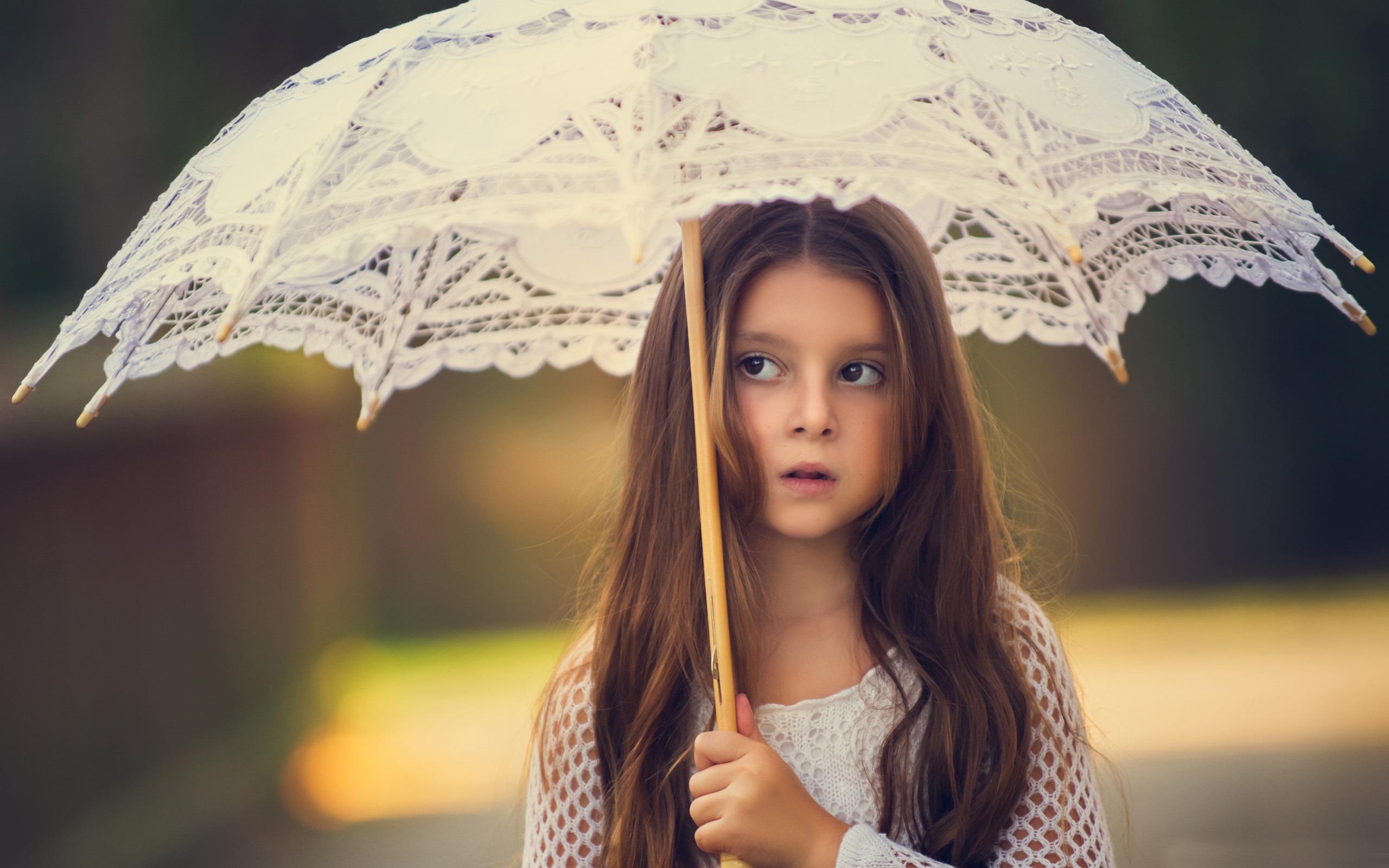 A little girl under a white umbrella looks away in surprise