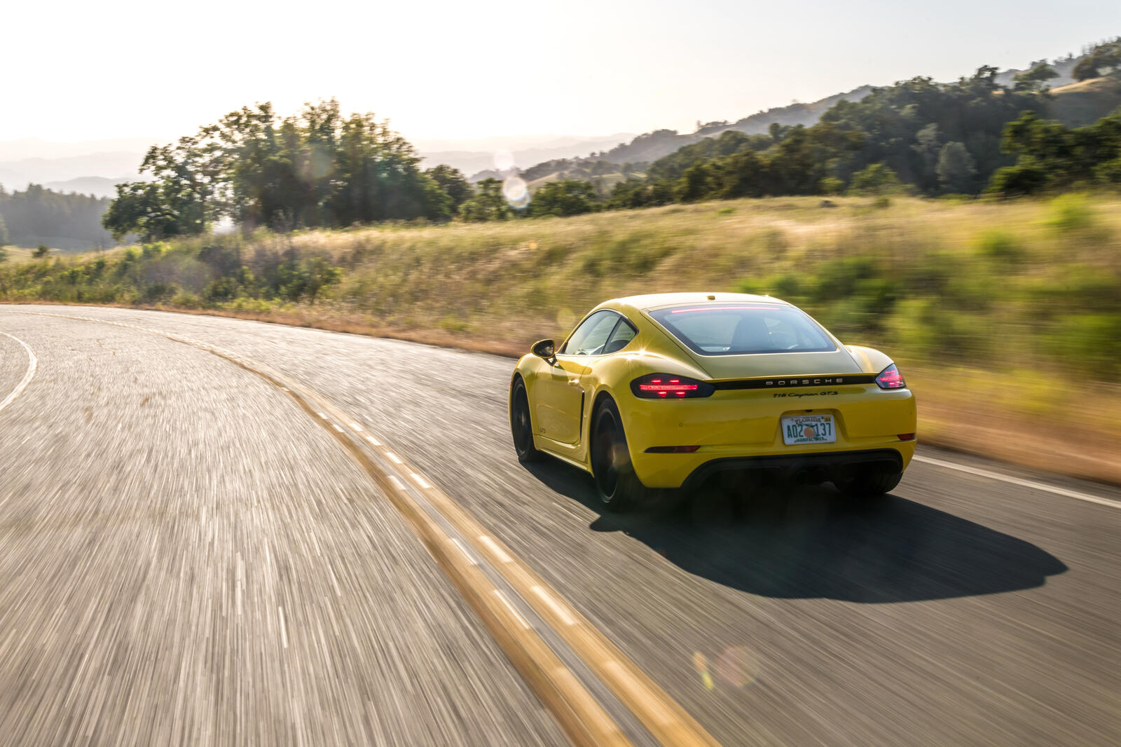 Бесплатное фото Желтый Porsche 718 едет по асфальтированной дороге