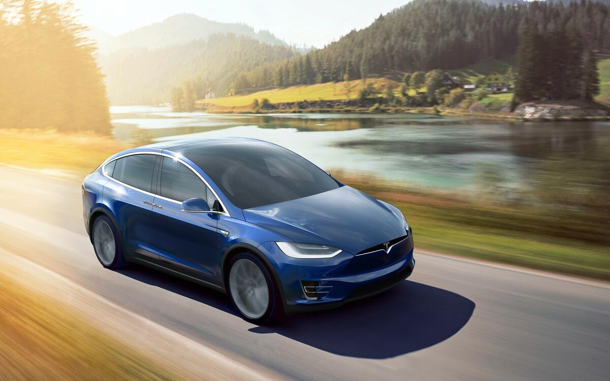 A Tesla Model X speeds down a highway with a river in the background