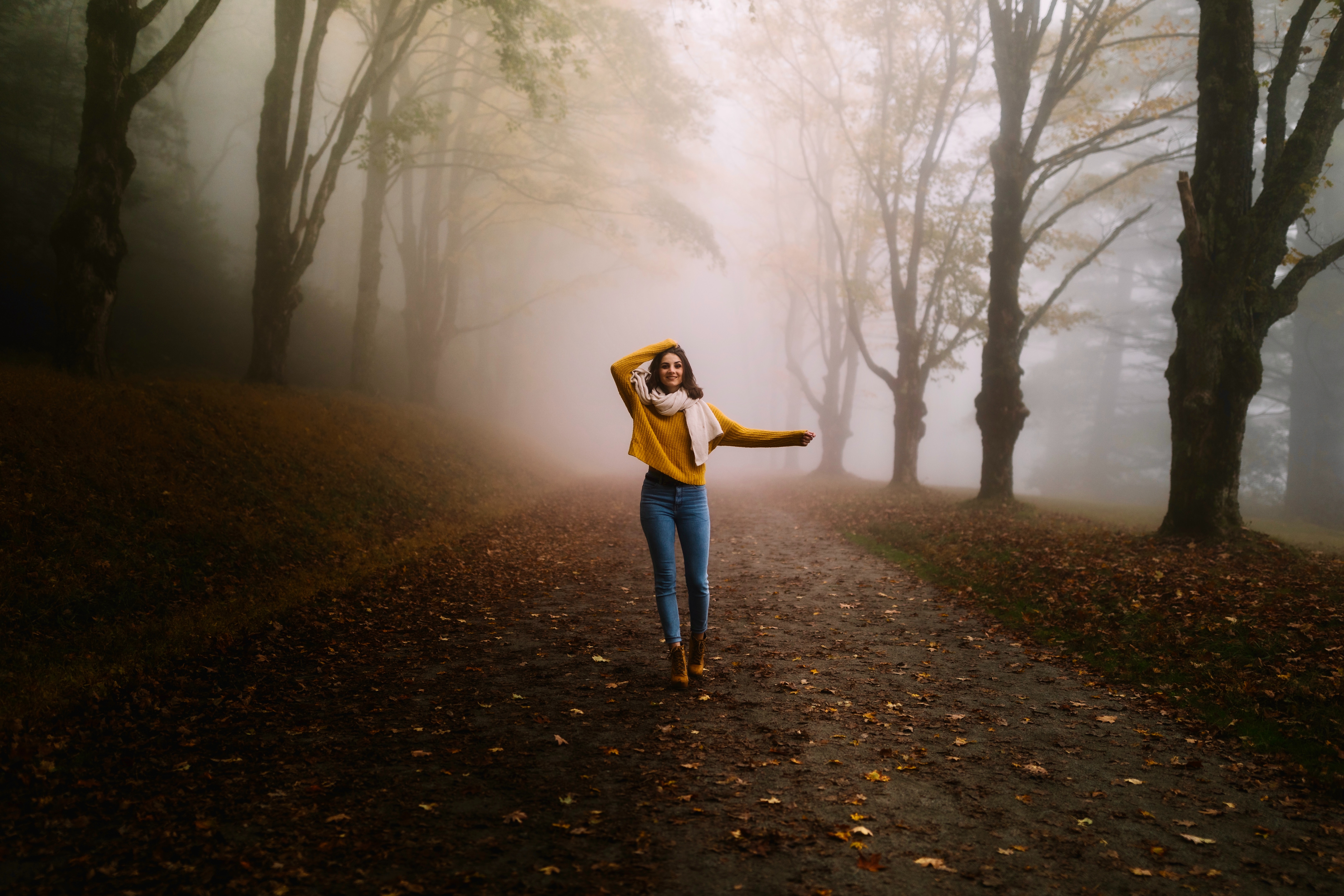 免费照片穿着黄色毛衣和牛仔裤的女孩在雾中的秋天的森林里