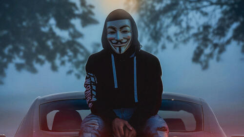 A guy in an anonymous mask sits on a car