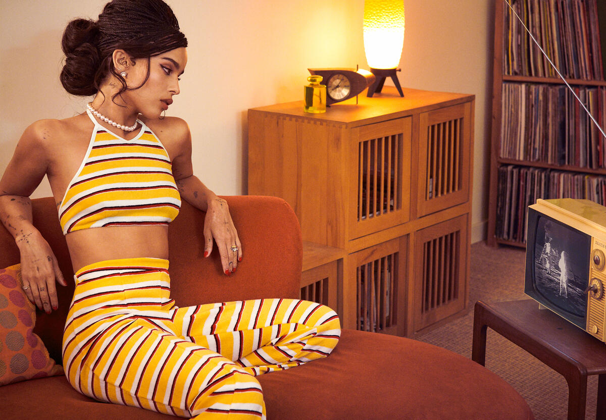 Zoe Kravitz sits on the couch in yellow and white summer clothes