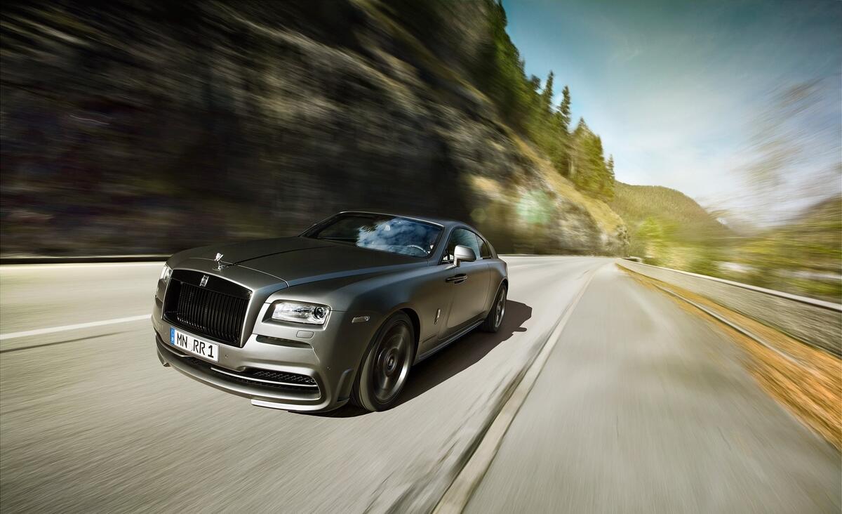 A gray Rolls Royce Wraith driving down a country road.