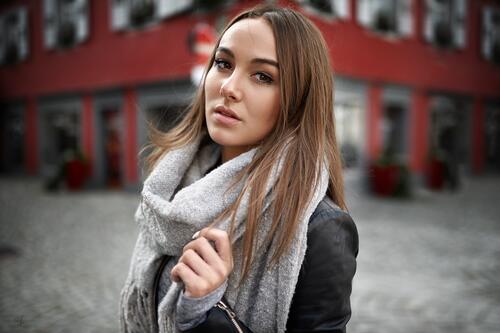 A brown-haired woman poses on the street with a light-colored scarf