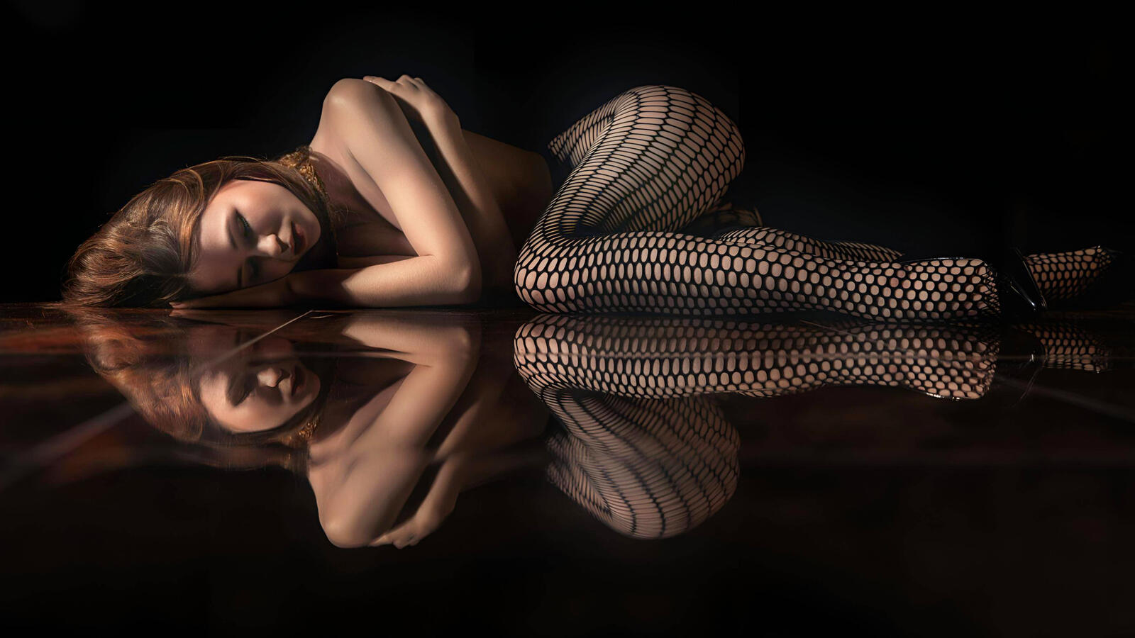 Free photo A girl lies on a mirrored floor in the darkness