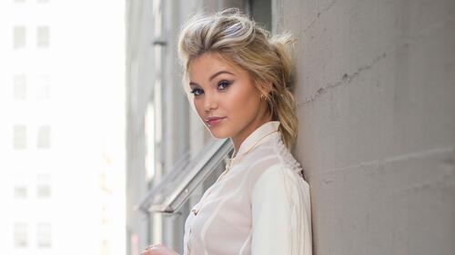 Olivia Holt is standing against the wall