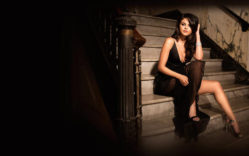Красивая брюнетка Селена Гомес сидит на лестнице в черном платье