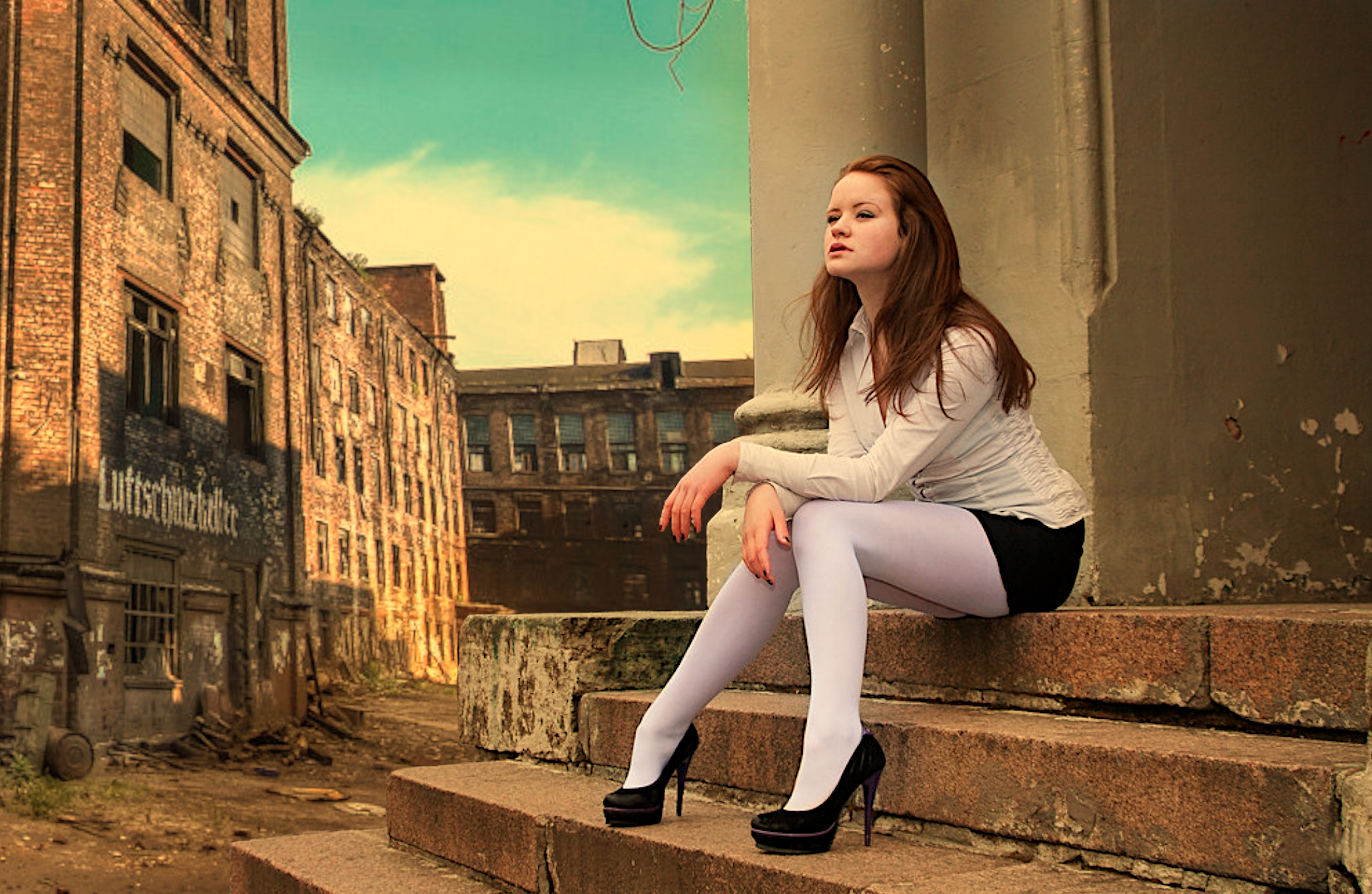 Бесплатное фото Рыжеволосая девушка в короткой юбке сидит на ступеньках