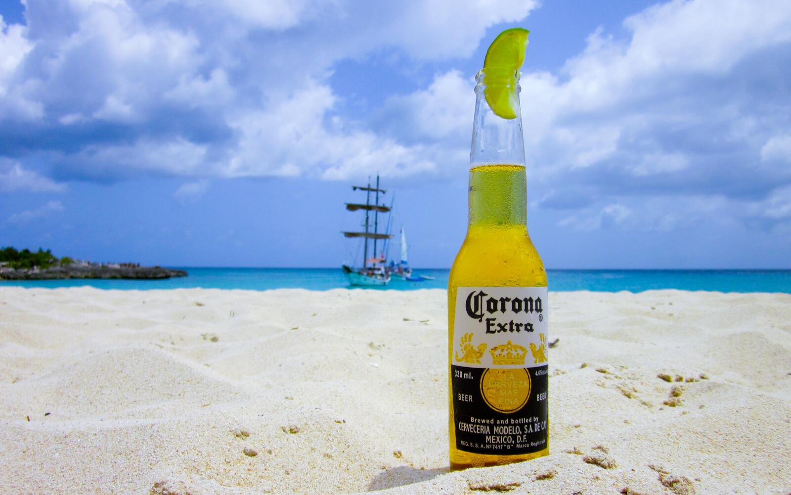 Free photo A bottle of crown on the white sand by the sea