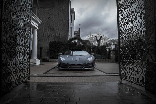 A matte black Lamborghini pulls into the courtyard of the mansion.