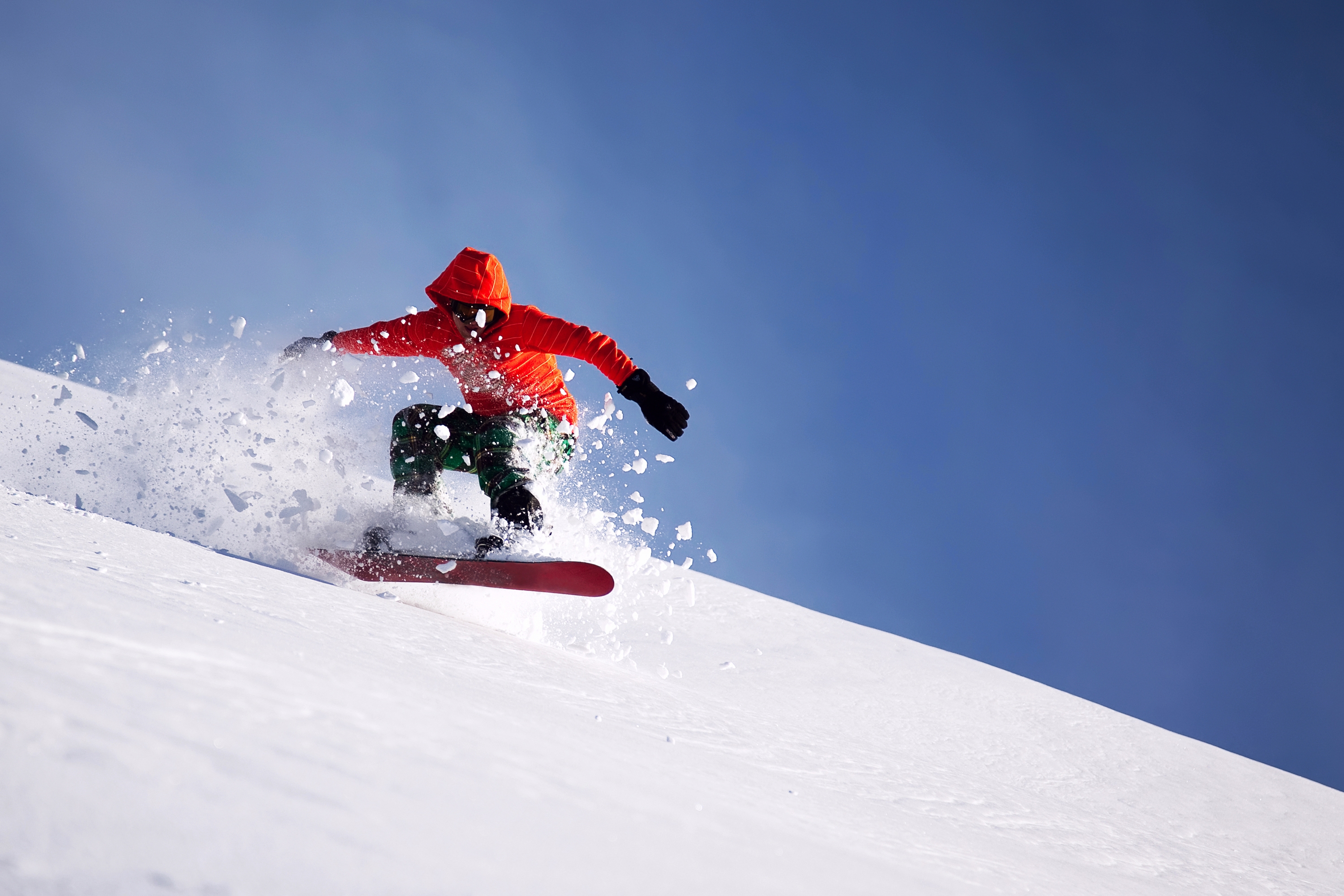 Мужчина скатывается с горы по снегу на сноуборде