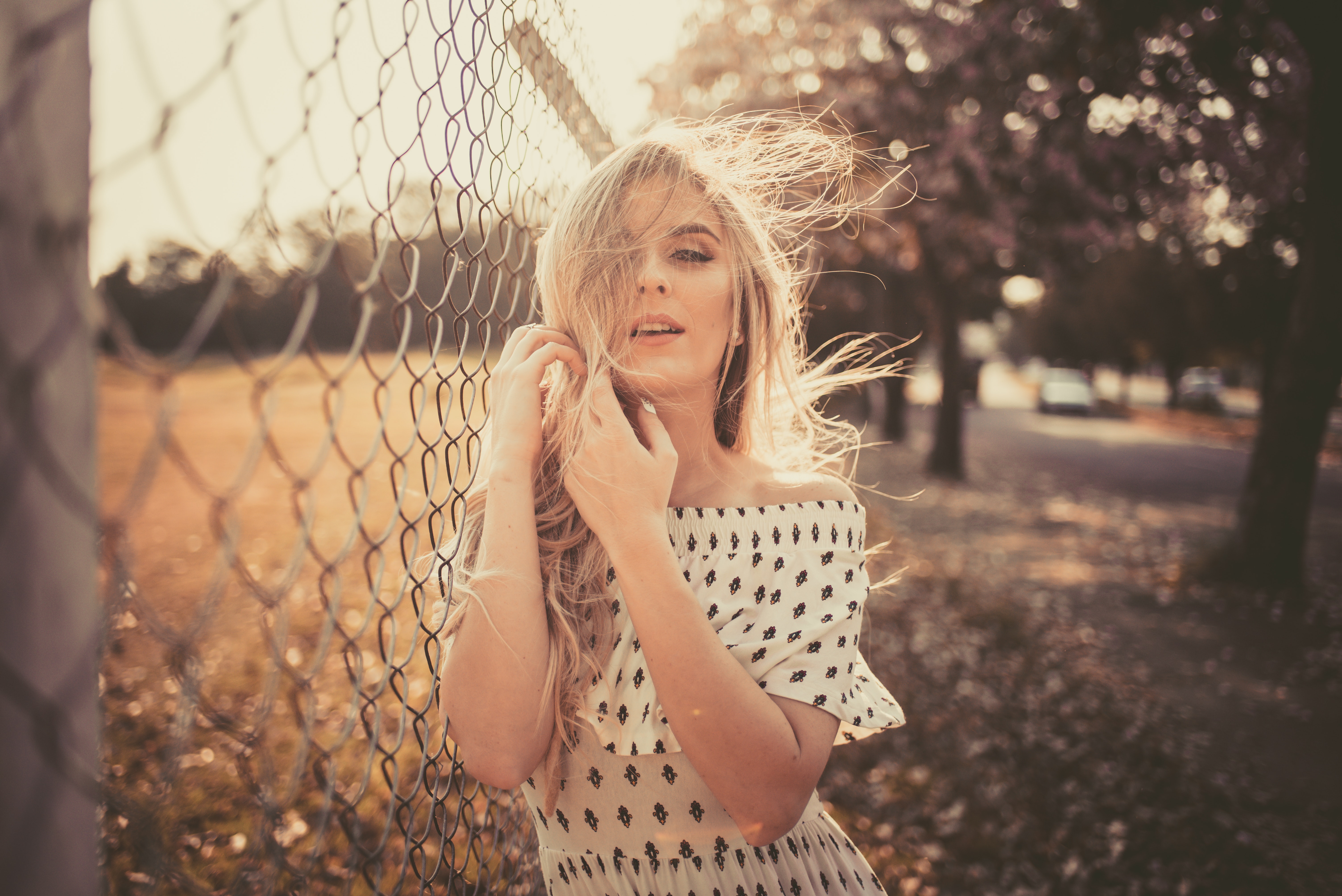 Free photo A blonde-haired girl in a light-colored dress stands at the fence