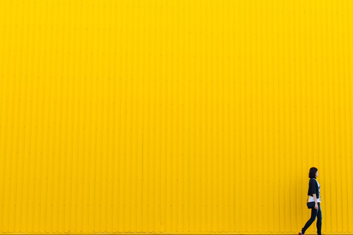 A girl walking against a yellow wall