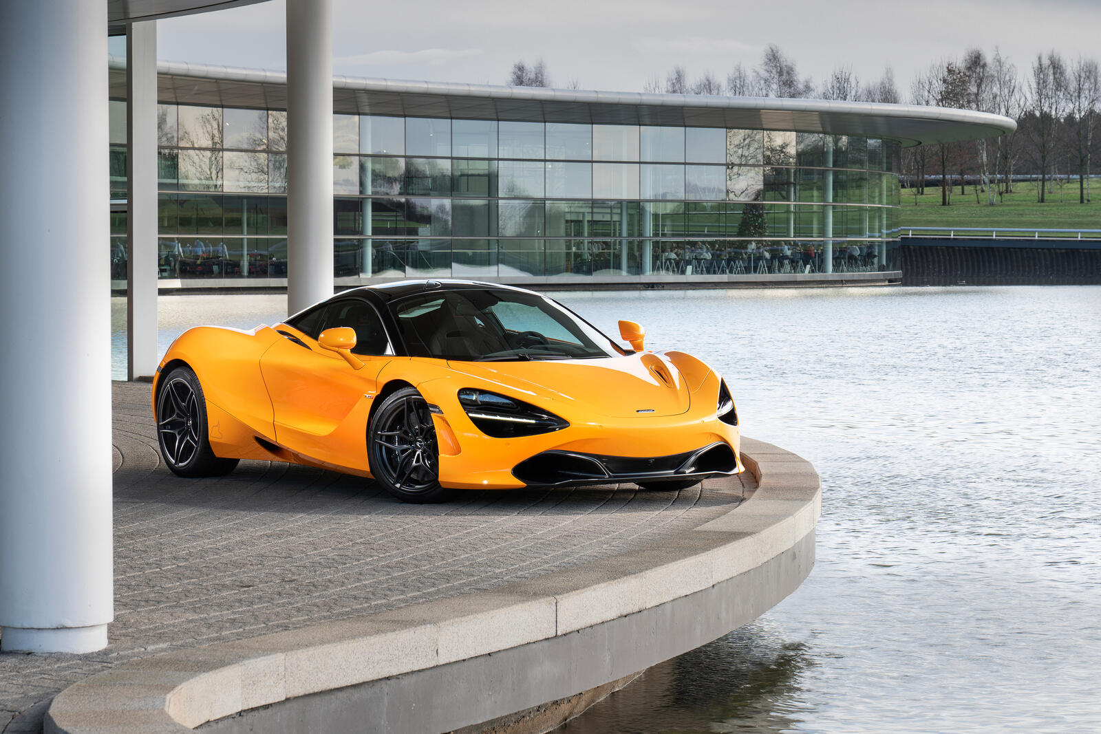 Free photo An orange Mclaren 720S stands by the water.