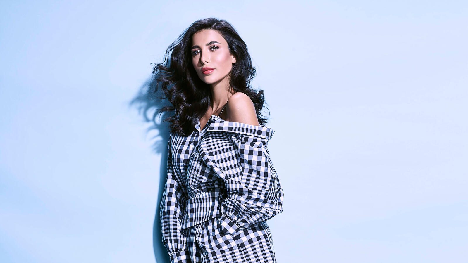 Free photo Dark-haired girl in a checkered coat poses on a blue background
