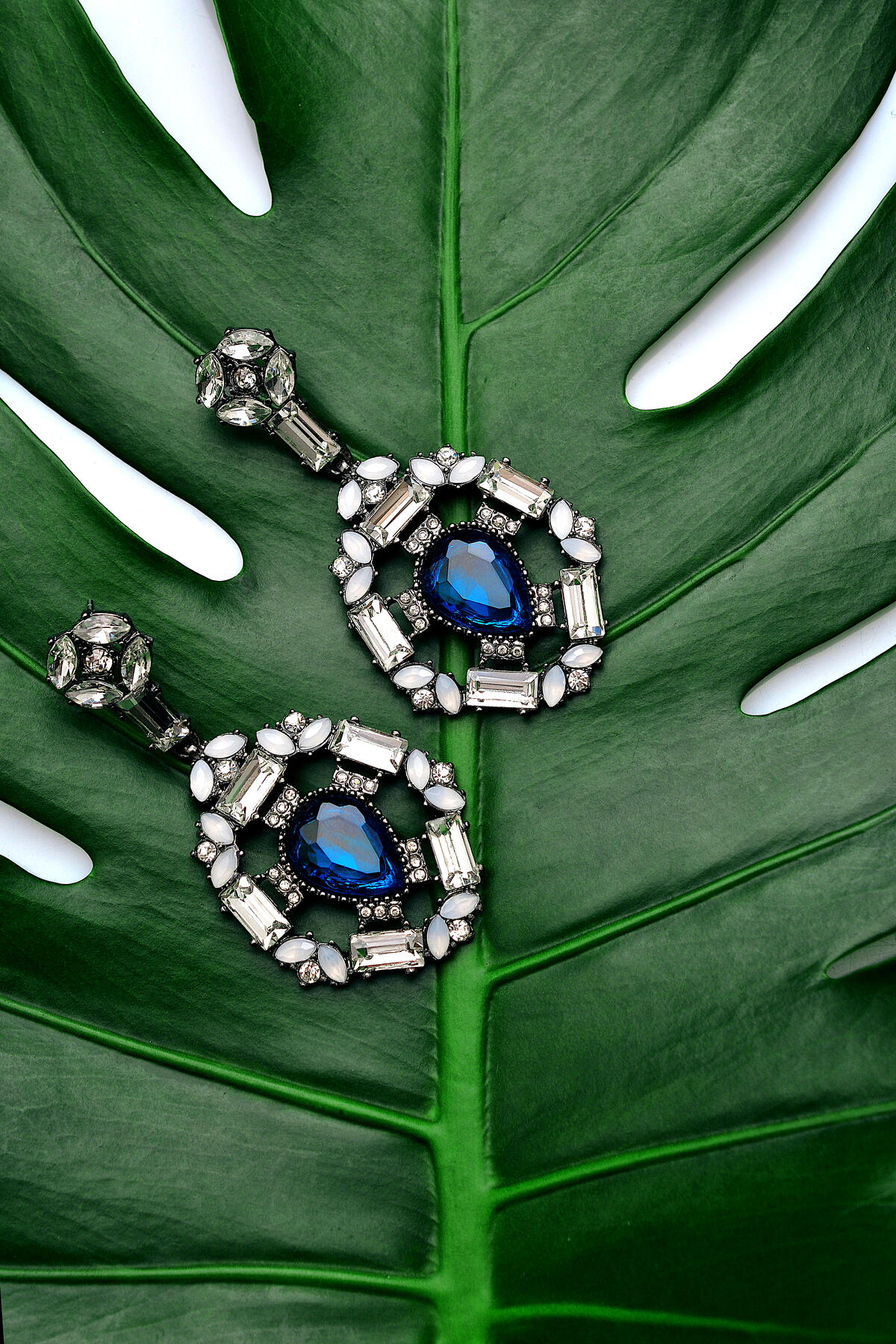 Earrings with a blue stone lie on a green leaf