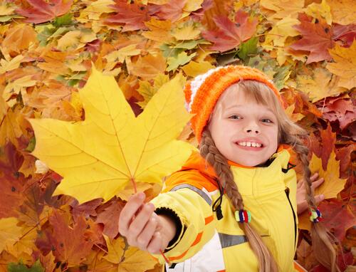 Девочка играет с опавшими листьями