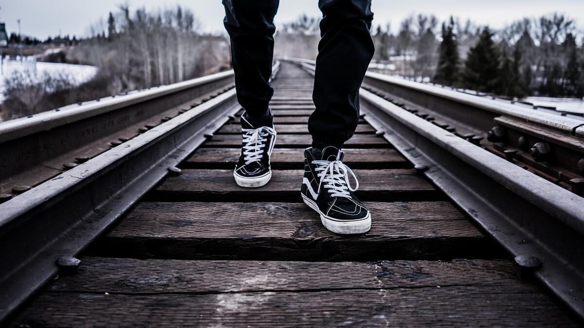 A man in sneakers is walking along the railroad tracks