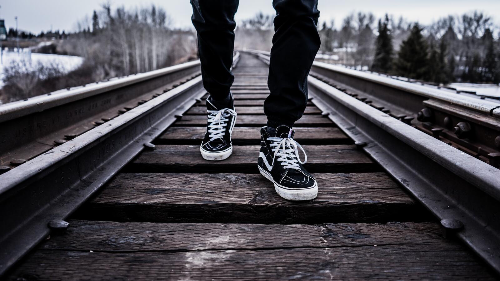 Free photo A man in sneakers is walking along the railroad tracks