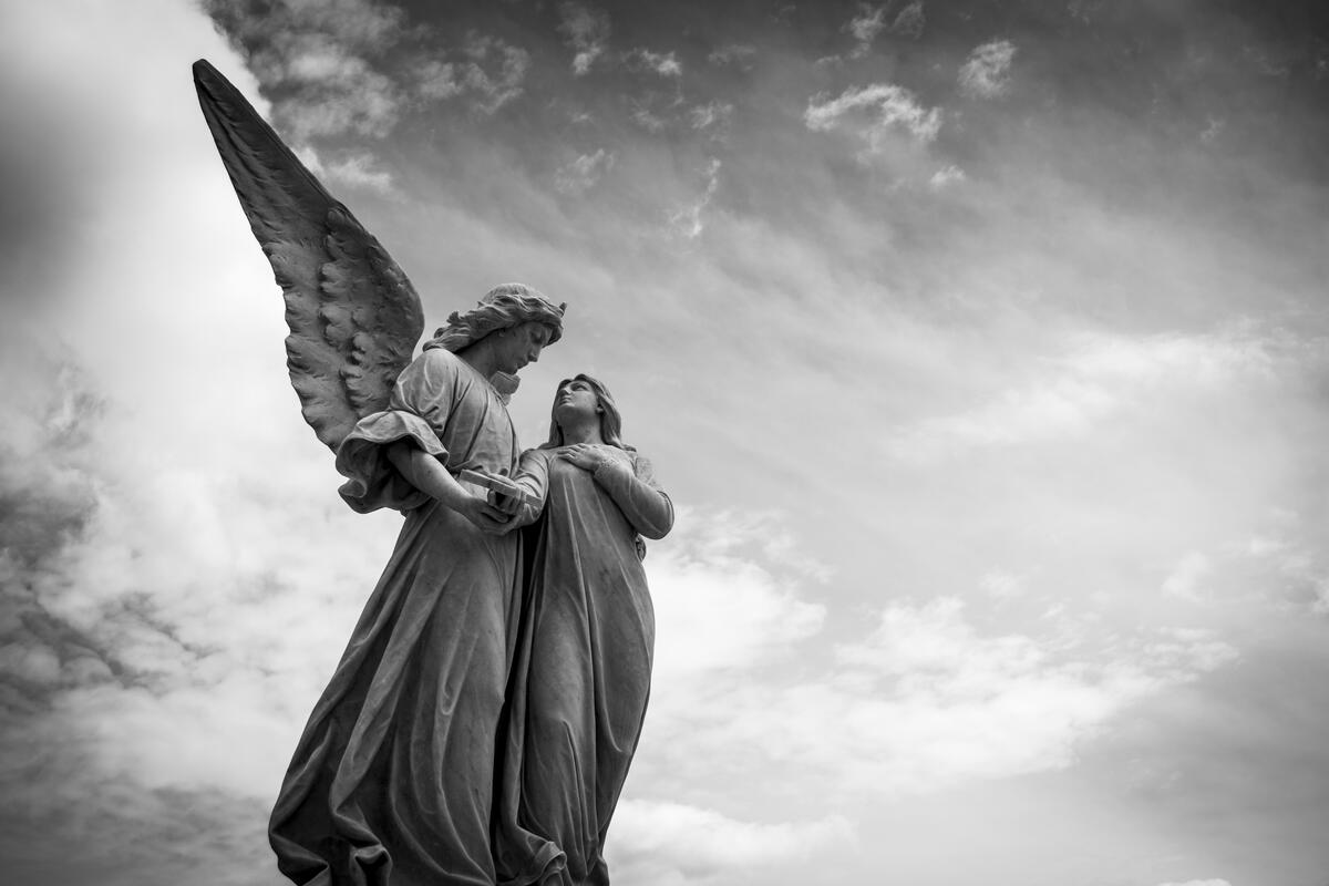 Статую ангела с крыльями держащего человека за руку