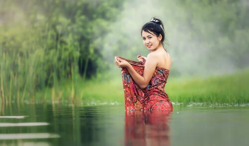 Азиатка в красном платье стоит в воде